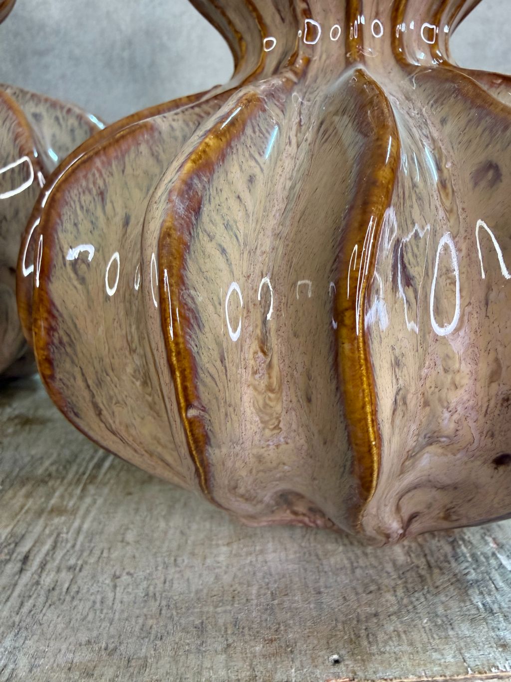 Twee glanzende keramieken vazen in bruin en oud roze met organische ribbelvorm op een houten ondergrond.