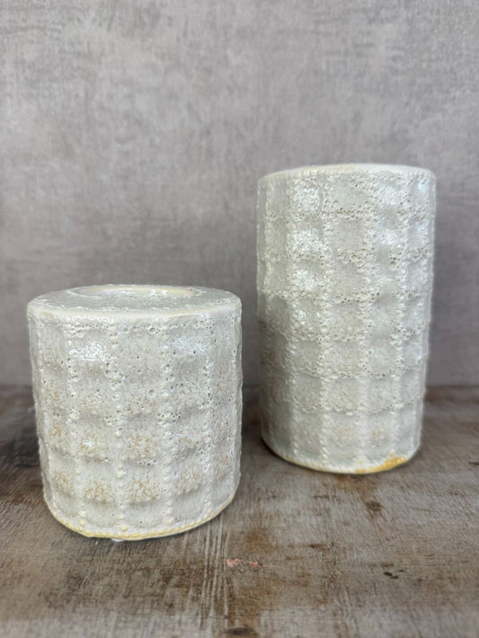 Twee keramieken waxinelichthouders in beige/grijs met lichte structuur en glans, geplaatst op een houten ondergrond.