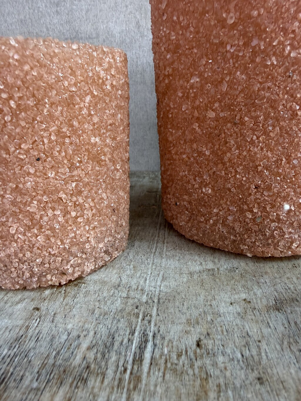 Twee oranje/zalmkleurige glazen waxinelichthouders met grove structuur op een houten ondergrond.