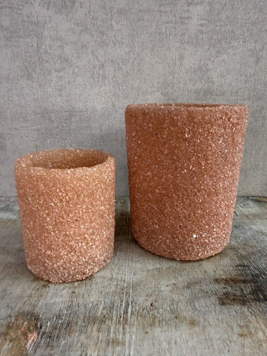 Twee oranje/zalmkleurige glazen waxinelichthouders met grove structuur op een houten ondergrond.