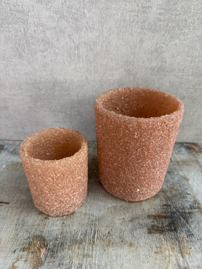 Twee oranje/zalmkleurige glazen waxinelichthouders met grove structuur op een houten ondergrond.