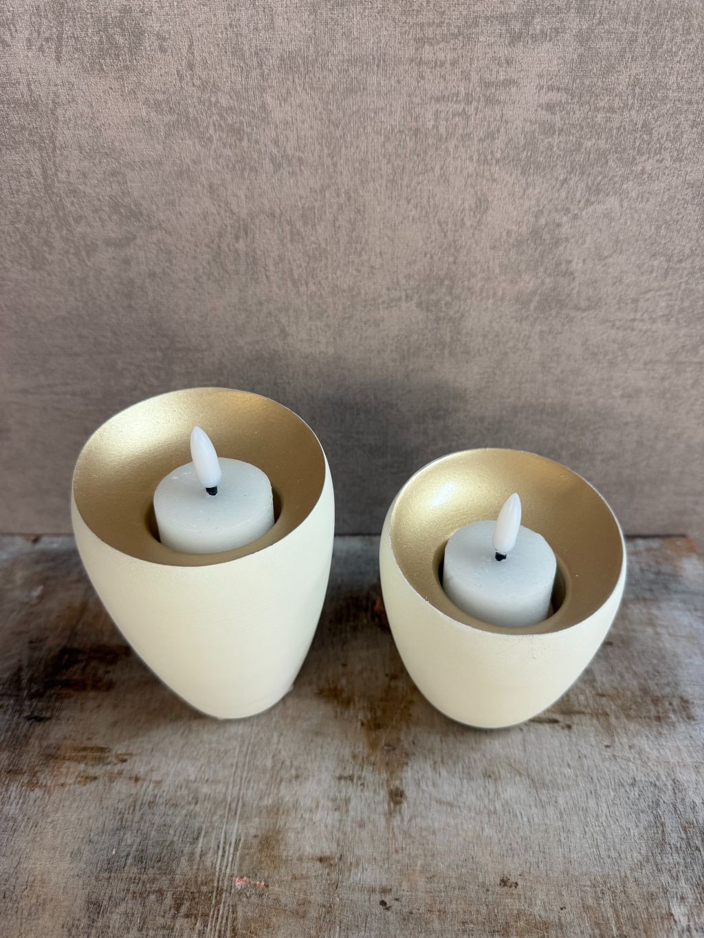 Twee waxinelichthouders Veroli in crème met gouden binnenzijde van Light & Living, in groot en klein formaat op houten oppervlak.