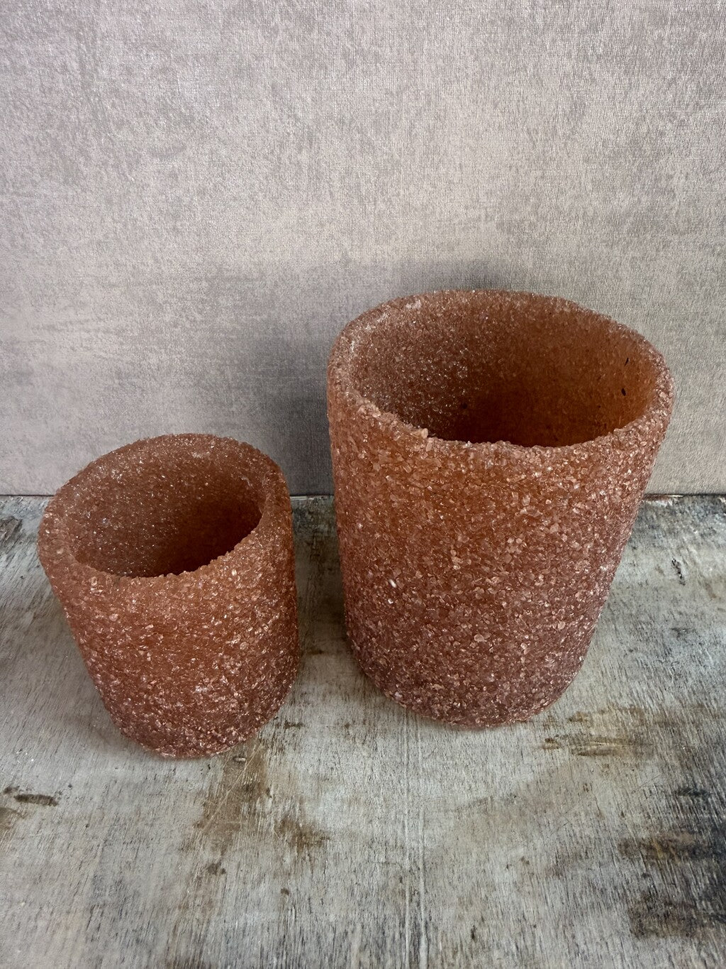 Bruine glazen waxinelichthouders met grove structuur in twee formaten op een houten ondergrond.