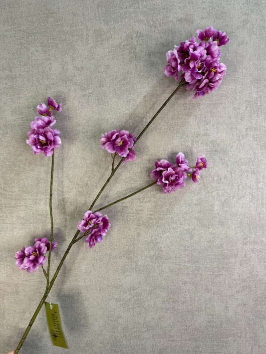Zijden bloesemtak Prunus met paarse bloesems, slanke vertakking en een natuurlijke uitstraling tegen een neutrale achtergrond.