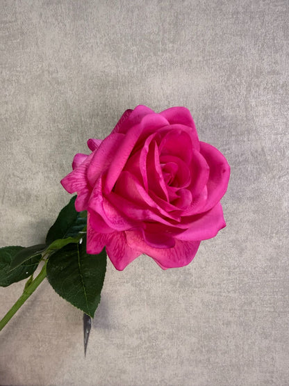 Fuchsia roze kunstroos met volle bloem en groene bladeren tegen een neutrale achtergrond.