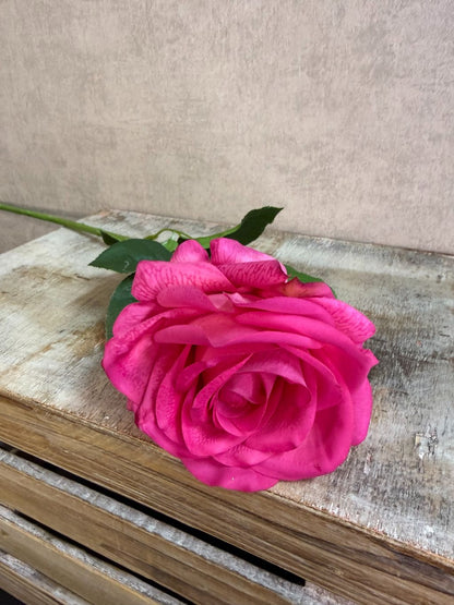 Fuchsia roze kunstroos met volle bloem en groene bladeren tegen een neutrale achtergrond.