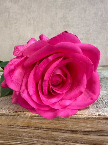 Fuchsia roze kunstroos met volle bloem en groene bladeren tegen een neutrale achtergrond.